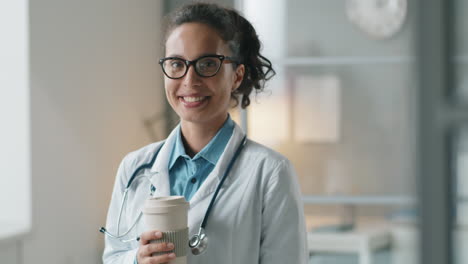 Portrait-of-Cheerful-Female-Doctor-Holding-Coffee-and-Smiling-at-Camera